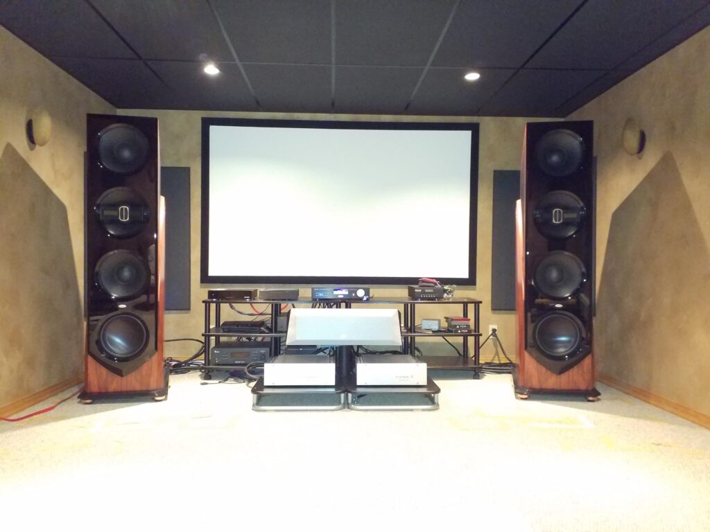 High-end audio setup featuring large speakers flanking a blank projection screen and audio equipment on a rack. Ideal for immersive home entertainment.